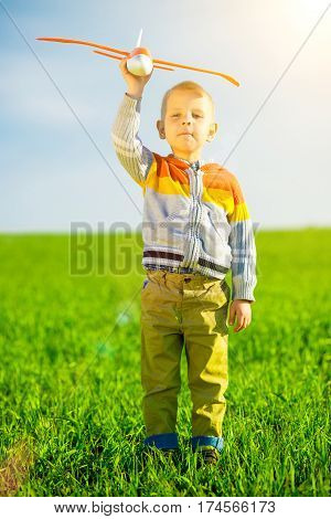 Happy kid playing with toy airplane against blue summer sky background.  Boy throw foam plane in green field. Best childhood concept.