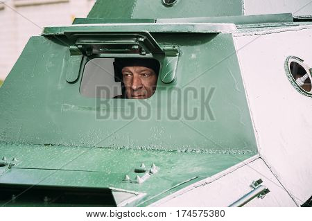 Pribor, Belarus - April 23, 2016: Re-enactor Dressed As Russian Soviet Crew Member Soldier Of World War II Looking Through Inspection Hatch Of The At Armoured Soviet Scout Car BA-64