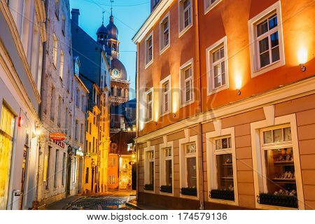 Riga, Latvia - July 1, 2016: View Of Deserted Narrow Cobbled Kramu Street Of Old Town In Bright Evening Illumination With Ancient Architecture Leading To Dome Cathedral Under Summer Blue Sky.