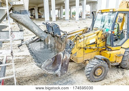 Concrete mixer truck is pouring fresh concrete into excavator bucket at construction site.