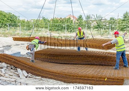 Zrenjanin Vojvodina Serbia - June 29 2015: Team of riggers assist mobile crane to unload reinforcing mesh on pile. Workers are helping in manage the cargo.