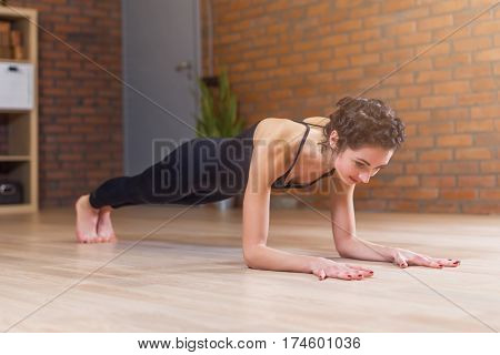 Fit woman doing yoga or pilates exercise standing in plank pose called phalankasana working out on floor in living room at home.