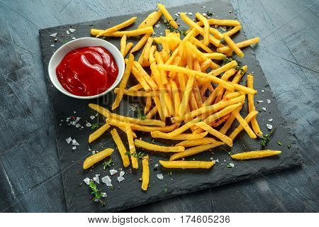 French fries with sea salt, cracked pepper and ketchup on stine board.