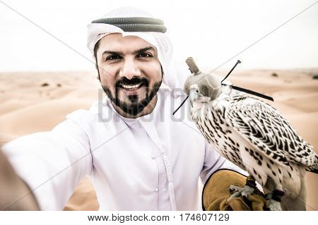 Arabic man with traditional emirates clothes walking in the desert with his falcon bird