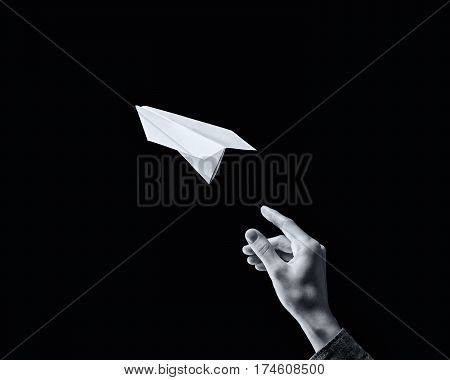 black and white image of a hand is throwing paper plane on black background.