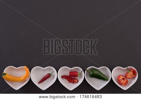 Different chili peppers on white plates, black stone background