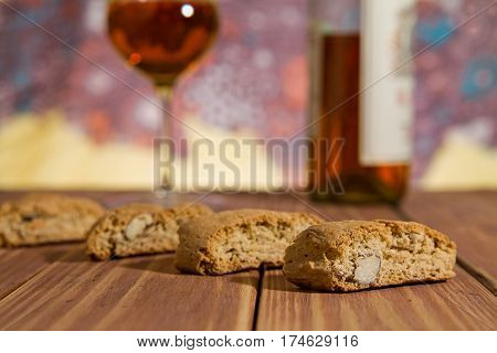 Closeup of Italian cantucci biscuits over a wooden table and a glass of vin santo wine on background