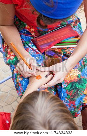 Woman paints boy hand with orange pencil during party