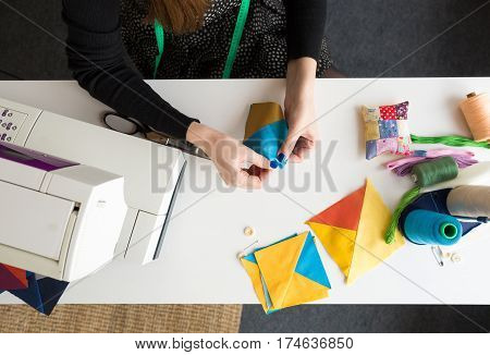 female hands holding color fabric pieces for patchwork quilt. tool kit for creation of a scrappy blanket on a white background: sewing machine, pieces of fabric, bobbin of thread, pins. flat lay.