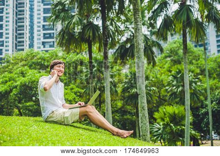 Man Businessman Or Student In Casual Dress Using Laptop In A Tropical Park On The Background Of Skys