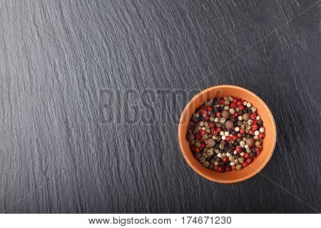 multicolored peppers peas in a clay cup on a slate boardHorizontal photo with free space area for text or design.