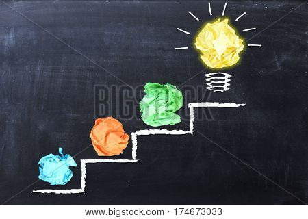 Evolving idea concept with colorful crumpled paper and light bulb on steps drawn on blackboard