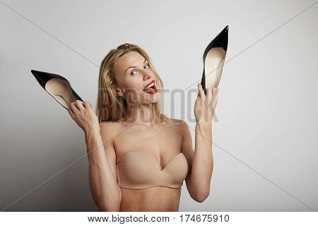Portrait of beautiful young woman with blonde hair holding black shoes in her hands.