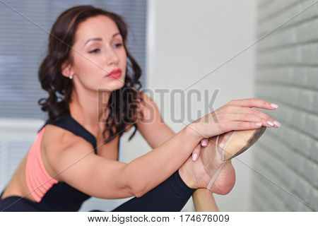 Ballerina stretches herself near barre in the classroom, focus on feet, shallow depth of field.