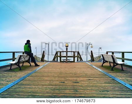 Man On Wooden Mole In Harbor Within Autumn Misty Day. Tourist At Handrail.
