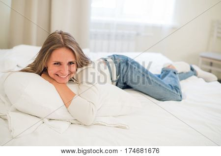 Smiling thoughtful pretty woman lying in bed at home.