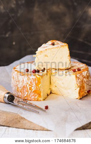German or French soft cheese with orange washed-rind cut off slice on waxed paper fork red pepper corns close up