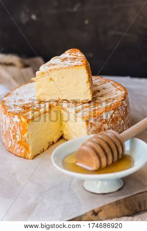 German or French soft cheese with orange mold rind on cutting board wood honey dipper close up rustic style