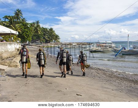 Dauin Philippines - 26 June 2016: The divers after the sea dive. Five young people in diving costumes on sand beach. Tropical nature landscape with divers. Sport on vacation