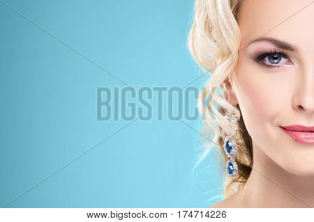 Half part portrait. Beautiful blond girl with luxury golden necklace over cyan background.