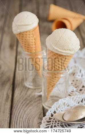 Vanilla ice cream in waffle cone on rustic wooden background