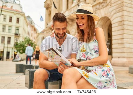 A beautiful young couple are sitting and holding a map and looking around at the Egyetem Square in Budapest, Hungary.