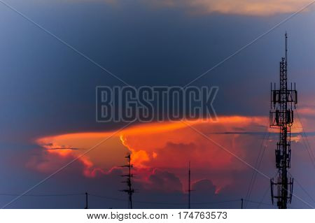 Sunset light shining through the clouds into the sky and the phone antenna.