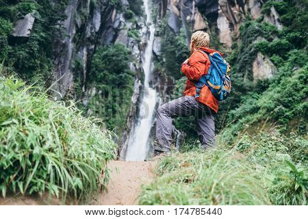 Tourist man with backback rest near the waterfall in rainy forest