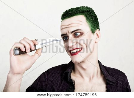 guy with crazy joker face holding knife, green hair and idiotic smike. carnaval costume.