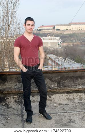 Photographing smiling Danila Mazić in a tight red shirt and black pants with his hands in the pockets of trousers in the background Petrovaradin fortress and the Danube River, Novi Sad, Serbia