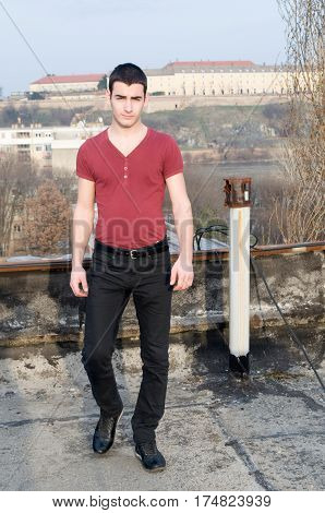 Photographing Danila Mazić in a tight red shirt and black pants with their hands beside the body a background Petrovaradin fortress and the Danube River, Novi Sad, Serbia