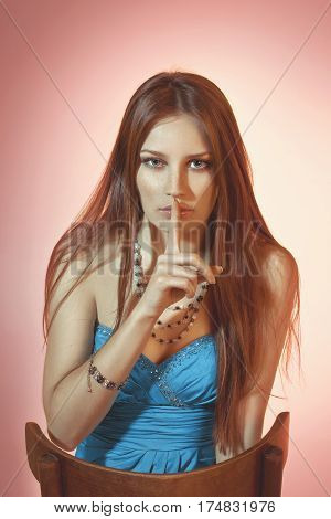 Beautiful colorful toned studio portrait of sensual young woman sitting on the chair with freckles soulful emotional eyes and long hair on rose background
