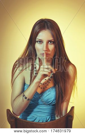 Beautiful colorful toned studio portrait of sensual young woman sitting on the chair with soulful emotional eyes freckles and long hair on yellow background