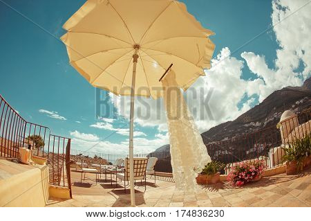Wedding dress under white sun umbrella on a background of sky and mountains