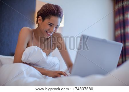Portrait beautiful young brunette woman sitting in bed. Black woman with laptop. Beautiful woman working on a laptop sitting on the bed in the house.