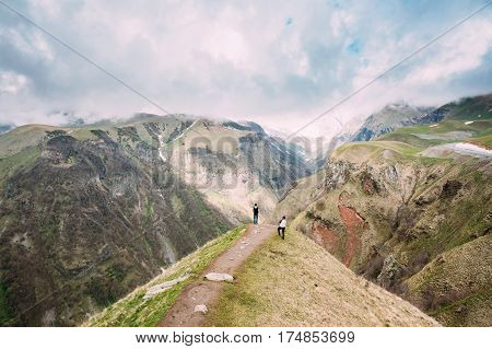 Two Tourists Are Photographed On Edge Of The Gudskoye Gorge In Georgia, Mtiuleti Region. Spring Mountain Landscape.