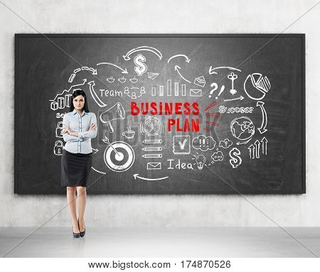 Portrait of a black haired woman standing with crossed arms near a blackboard with a white and red business plan sketch on it.