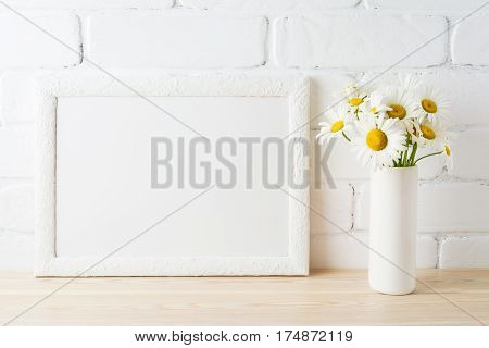 White landscape frame mockup with daisy flower in styled vase near painted brick wall. Empty frame mock up for presentation design. Template framing for modern art.