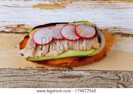 Sandwiches with herring, pickled cucumbers, radish, and onion on cutting board