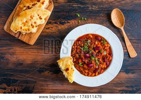 Traditional Polish dish stewed Breton beans with minced beef bacon mashed tomatoes onion garlic paprika bay leaves and spices. White plate and bread on wooden rustic table top view.