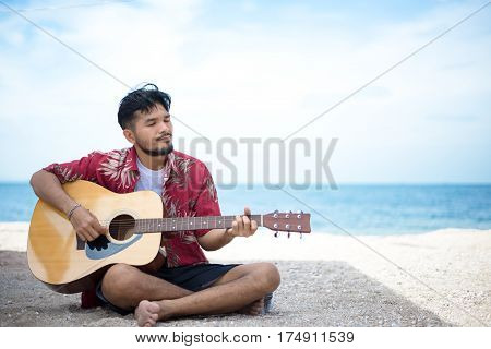 Handsome man playing classic guitar sitting on the beach in vacations