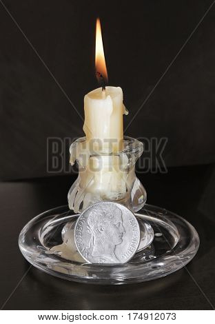 Close up view of old fashioned glass candlestick with a burning candle and vintage French 5 Francs silver coin with Napoleon Bonaparte portrait.