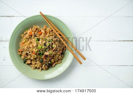 Plate of basil fried rice viewed from above with some chopsticks on the side. This asian inspired recipe uses lots of fresh ingredients like basil carrots onions and there's also fried eggs and chicken.