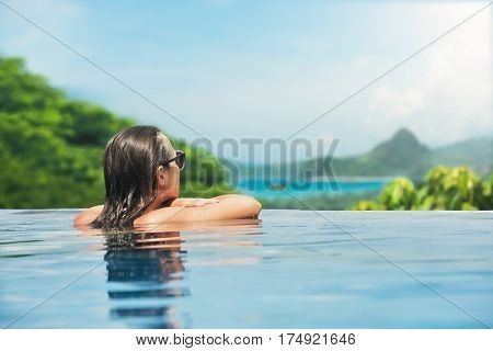 Pretty young sexy woman enjoying resting on the edge of outdoor swimming pool on background green mountains. Travel happiness emotion summer holiday concept.
