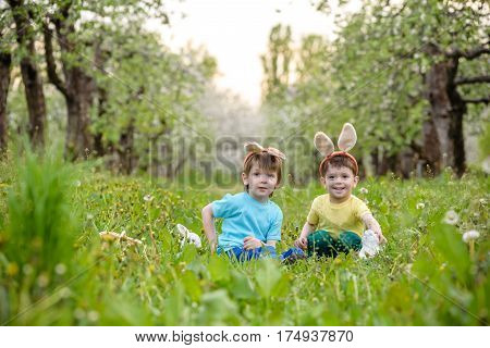 Two Little Kids Boys And Friends In Easter Bunny Ears During Traditional Egg Hunt In Spring Garden,