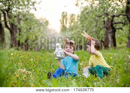 Two Little Kids Boys And Friends In Easter Bunny Ears During Traditional Egg Hunt In Spring Garden,