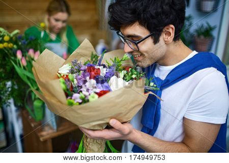Happy young man smelling multi-floral bouquet in flower-shop