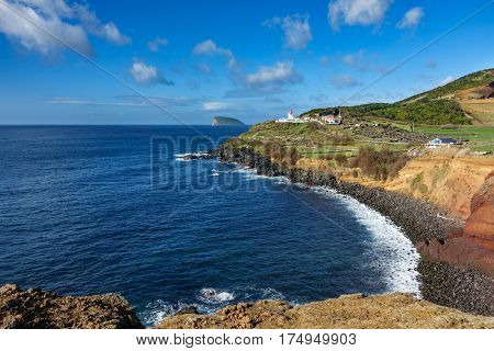 Wide angle view of volcanic coast, lighthouse and goat island in Terceira, Portugal