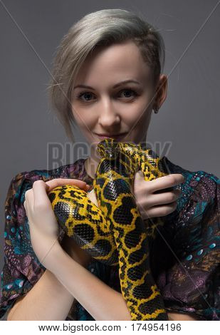Young woman holding yellow anaconda on gray background