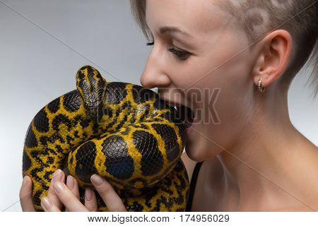 Woman biting yellow snake on gray background